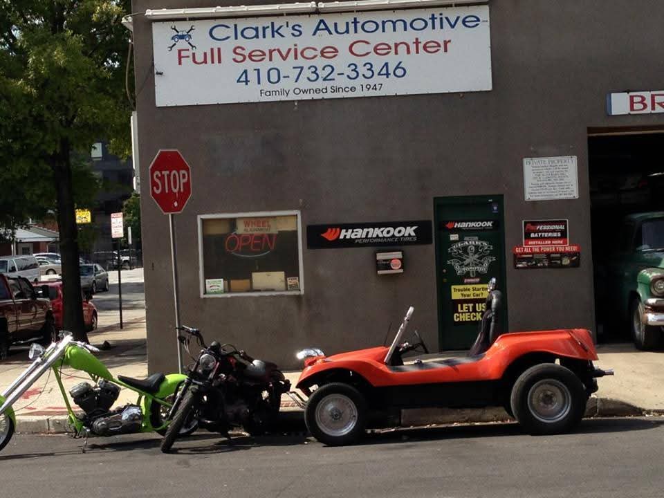 The Clark's Automotive shop in Baltimore, with its Full Service Center sign reading 410-732-3346 and Family Owned Since 1947 above the open service bay, a chopper motorcycle and an orange dune buggy parked at the curb.